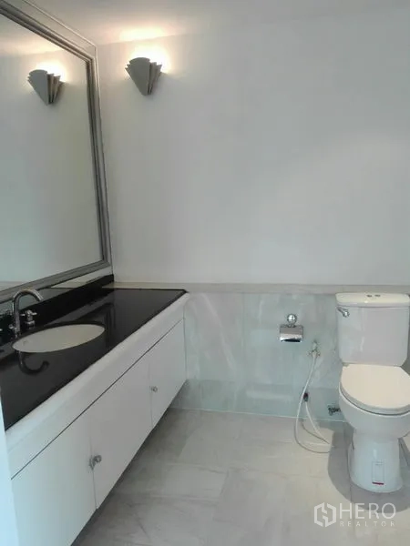 Condominium for rent in Khlong Toei, Bangkok - Guest bathroom with large mirror, countertop sink, and toilet in light tones.