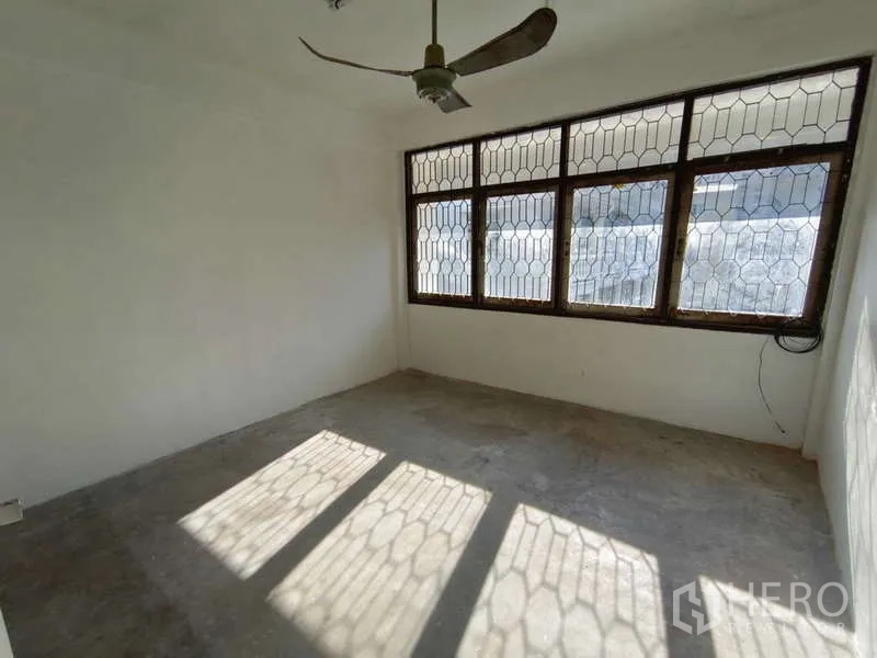 Shophouse for rent in Bang Na, Bangkok - Sunlit room with security-grilled windows and concrete floor.