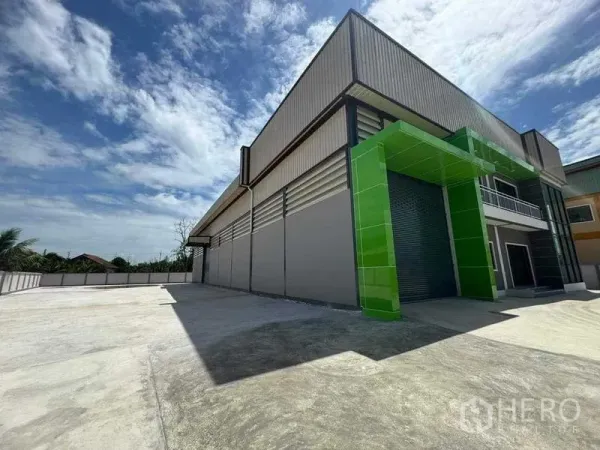 Factory for sale in Samut Sakhon - Loading bay framed in green panels with oversized roller shutter and expansive yard.