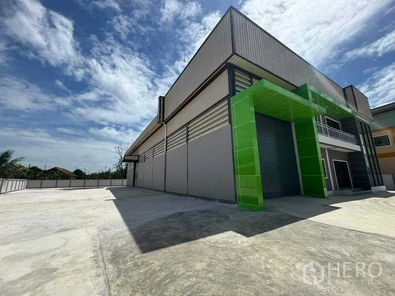 Factory for sale in Samut Sakhon - Loading bay framed in green panels with oversized roller shutter and expansive yard.