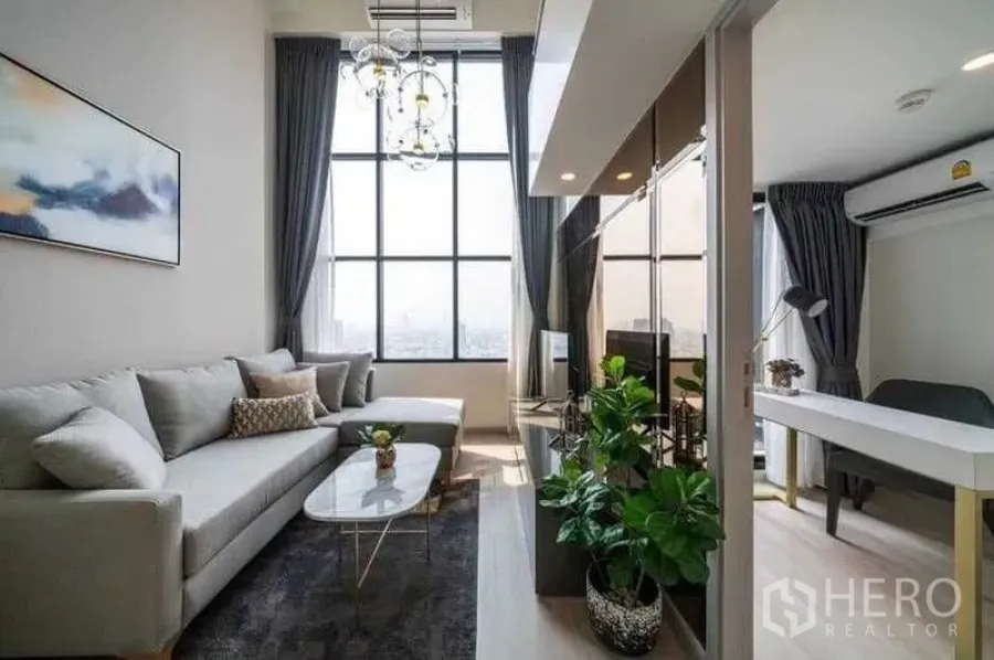 Condominium for rent in Sathon, Bangkok - Bright living room with L-shaped sofa, double-height windows and adjacent work area.