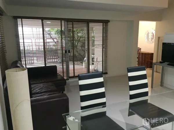 Detached House for rent in Watthana, Bangkok - Open-plan living and dining room with glass table, leather sofa and sliding doors to the patio.