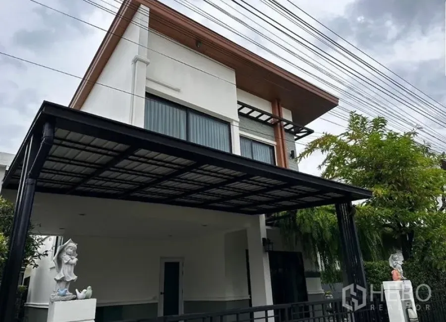 Detached House for rent in Prawet, Bangkok - Alternate exterior angle of the modern two-storey house with carport and trees.