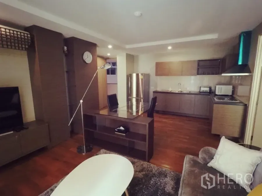 Condominium for rent or sale in Khlong Toei, Bangkok - Spacious lounge featuring TV unit, work desk and a full kitchen with stainless refrigerator and range hood.