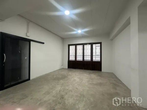 Home Office for rent in Pathum Wan, Bangkok - Spacious studio area with concrete flooring, barred windows and a black-framed sliding glass door.