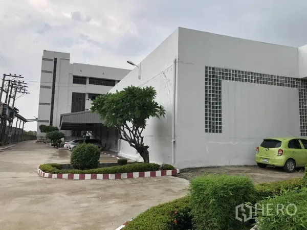 Factory for rent in Lat Krabang, Bangkok - Modern white factory exterior with wide driveway, landscaped shrubs and parking area in Lat Krabang.