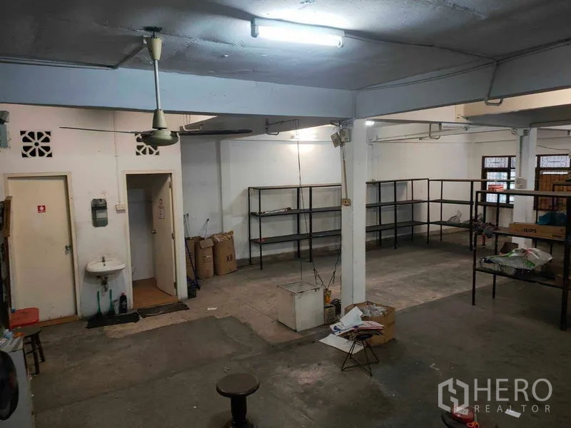 店屋 出租在Watthana, Bangkok - 后勤仓储区，水泥地、吊扇、洗手池与金属置物架。