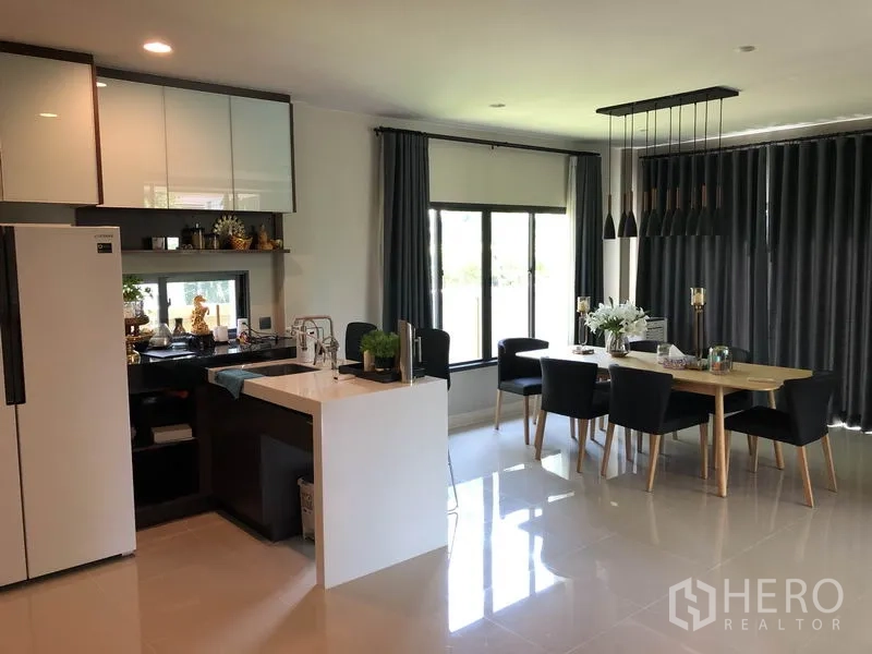 Detached House for rent in Bang Kapi, Bangkok - Bright kitchen with island and cabinets beside a dining area and full-height curtains.