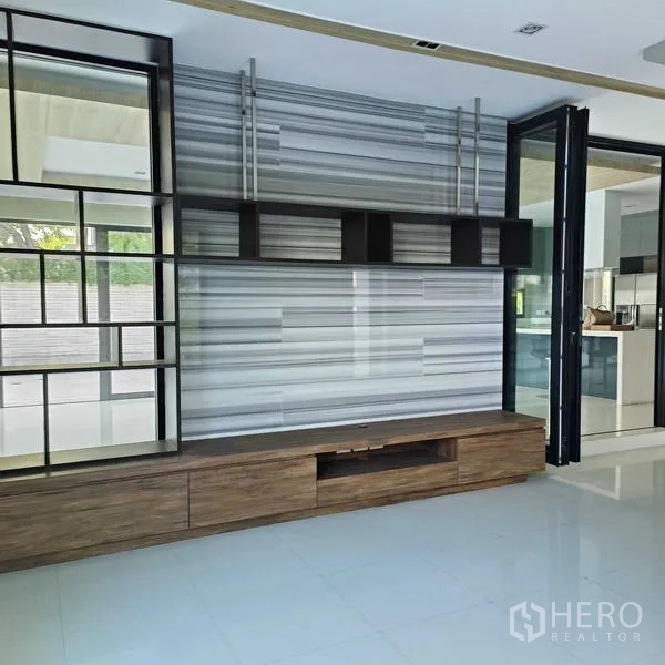 Detached House for rent or sale in Mueang Nonthaburi, Nonthaburi - TV feature wall with shelving next to glass partitions leading to the kitchen.