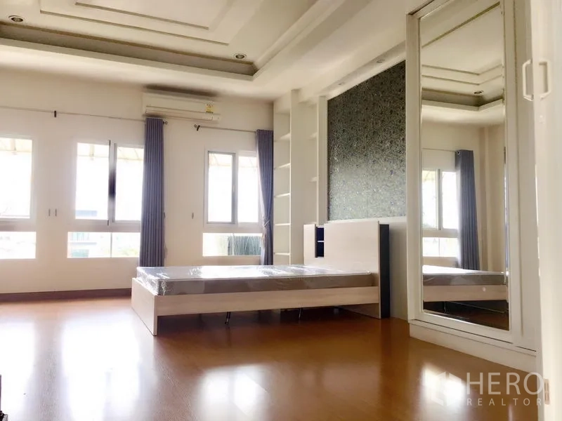 Townhouse for rent in Prawet, Bangkok - A sunlit large bedroom with a mirrored wardrobe and multiple windows.