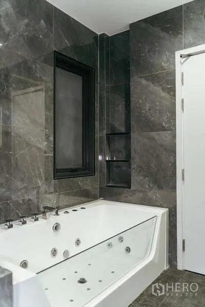 Detached House for sale in Sai Mai, Bangkok - Bathroom clad in marble tiles with a white jacuzzi bathtub and black framed window.
