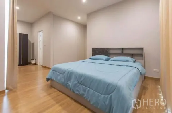 Detached House for rent or sale in Lat Phrao, Bangkok - Spacious bedroom with wood flooring, recessed lighting and blue bedding.