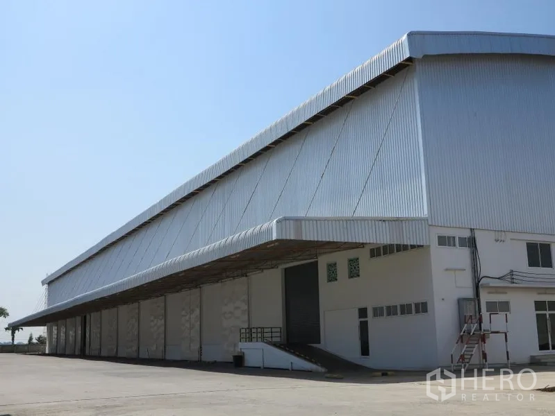 Warehouse for rent in Lopburi - Large metal-clad warehouse exterior with covered loading bays and a ramp under a clear sky
