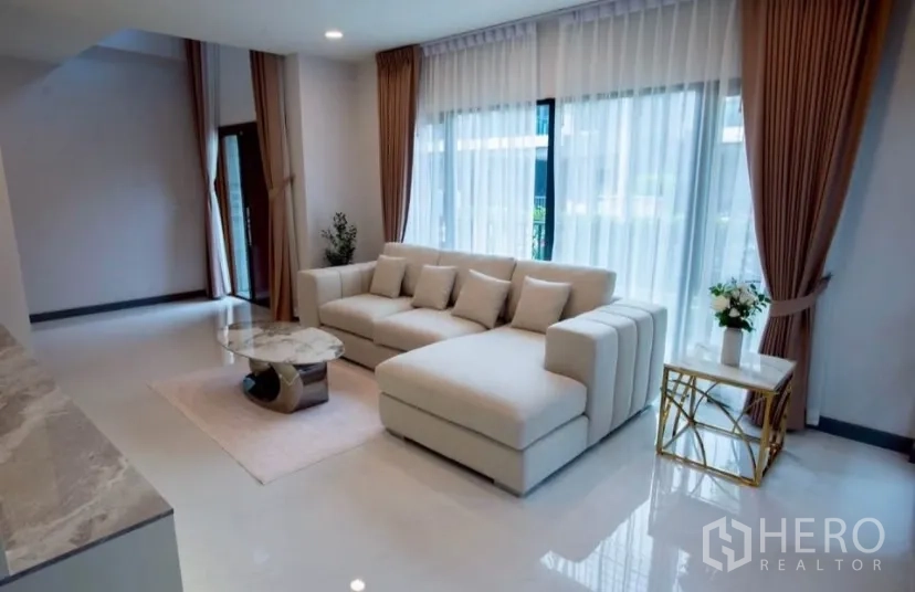Detached House for rent in Bang Phli, Samut Prakan - Sunlit lounge with large windows, sheer curtains and a sectional sofa.
