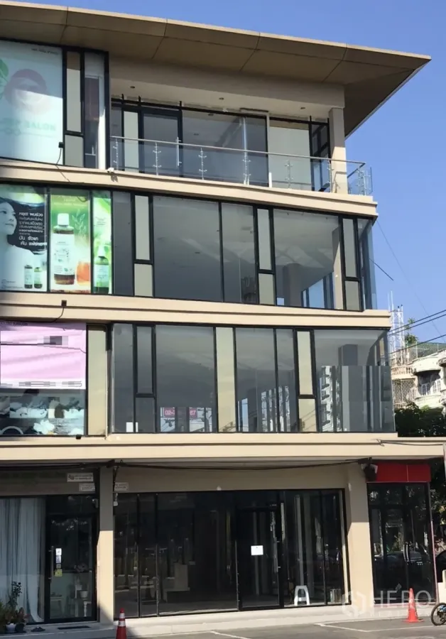 Retail Space for rent in Suan Luang, Bangkok - Modern multi-storey commercial building with full-height glass storefronts, an upper-floor balcony and parking area in front under a clear sky.