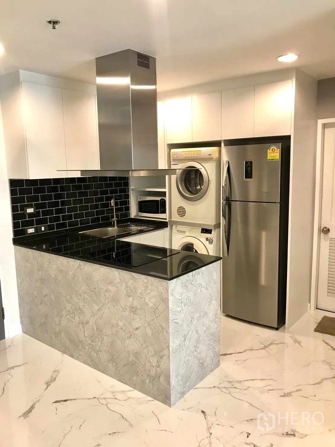 Condominium for rent or sale in Khlong Toei, Bangkok - Compact kitchen with black tile backsplash, induction hob, stainless refrigerator and washer-dryer.