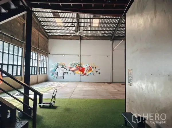 Warehouse for rent in Khlong Toei, Bangkok - View from stairs to an open warehousing space with turf area and a mural on the end wall.