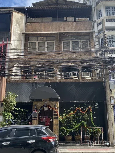 Shophouse for sale in Khlong Toei, Bangkok - Street view of a multi-storey brick shophouse with arched balconies, shopfront, potted plants and overhead power lines in Khlong Toei.