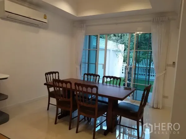 Townhouse for rent in Mueang Samut Prakan, Samut Prakan - Bright dining room with wooden table and sliding glass doors opening to green garden.