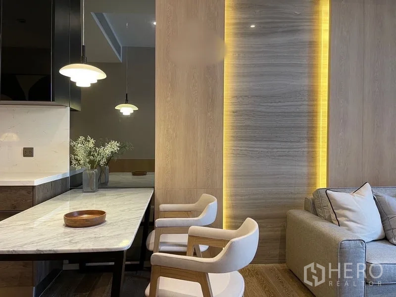 Condominium for rent or sale in Pathum Wan, Bangkok - Close-up of marble dining counter with two chairs beside a backlit wood and stone accent wall.