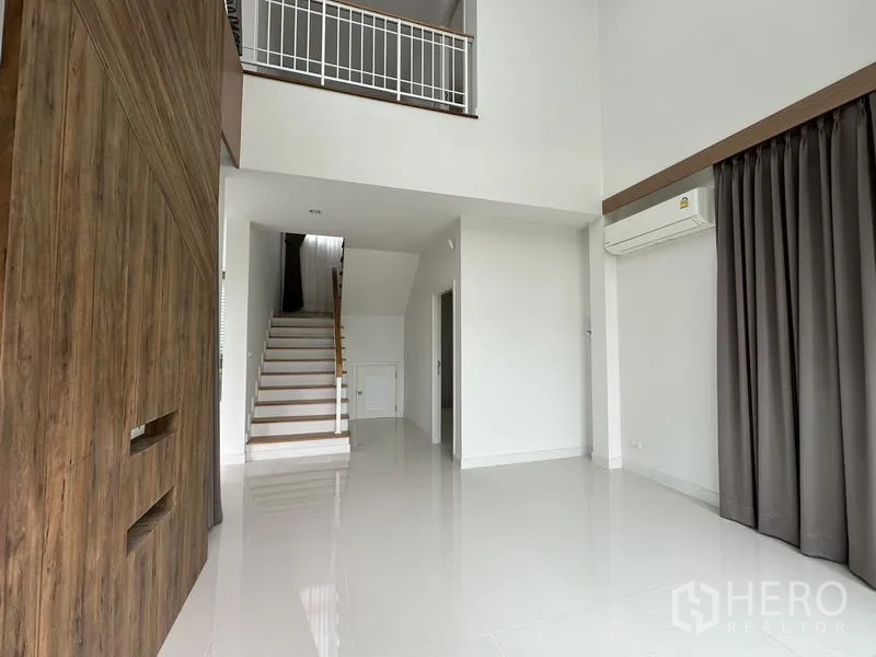 Detached House for sale in Lam Luk Ka, Pathum Thani - Open-plan lounge showing the staircase to the upper floor and mezzanine railing.