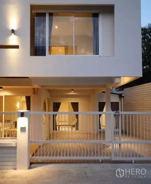 Townhouse for rent or sale in Watthana, Bangkok - Front view of townhouse with large sliding window above and secure metal gate to driveway.