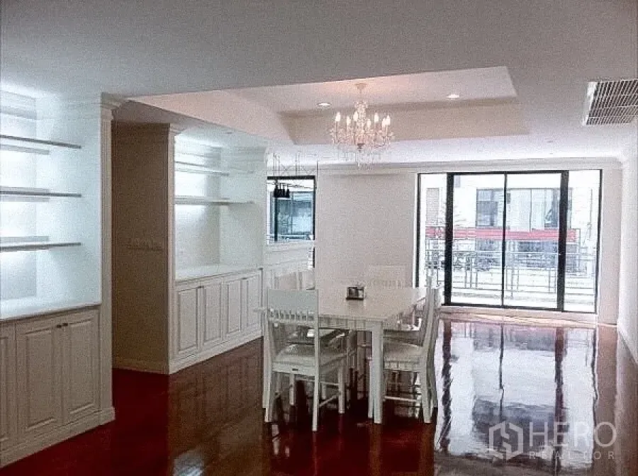 Townhouse for rent in Khlong Toei, Bangkok - Bright dining area with chandelier, built‑in cabinets, glossy wooden floors and sliding doors to a balcony.