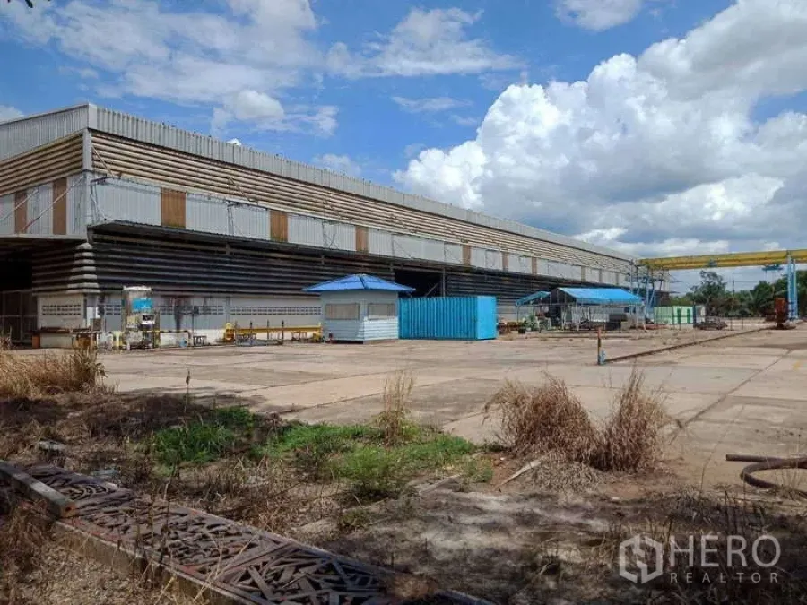 工厂 出售在Chachoengsao - 修长的工业厂房面向开阔院场与移动门式起重机，天空云层壮观。
