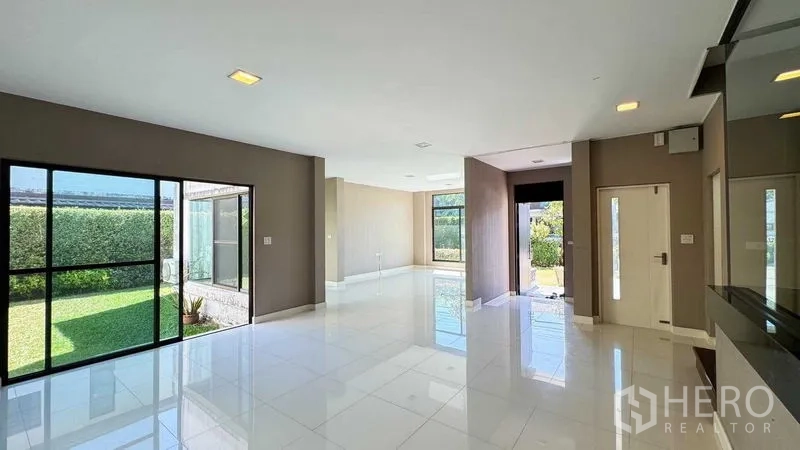 Detached House for sale in Bang Kapi, Bangkok - Open-plan living and dining area with large windows and glossy white tiles overlooking the lawn.
