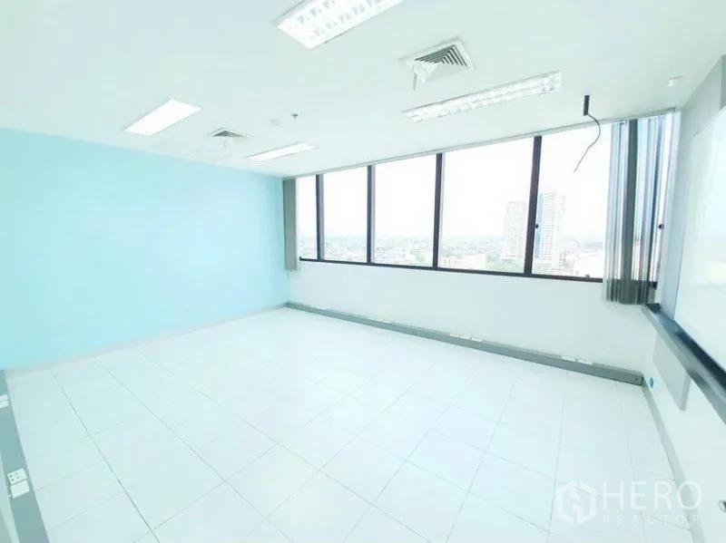 办公空间 出租在Bang Na, Bangkok - 开阔办公室，整排窗户与蓝色墙面，享城市天际线景观。