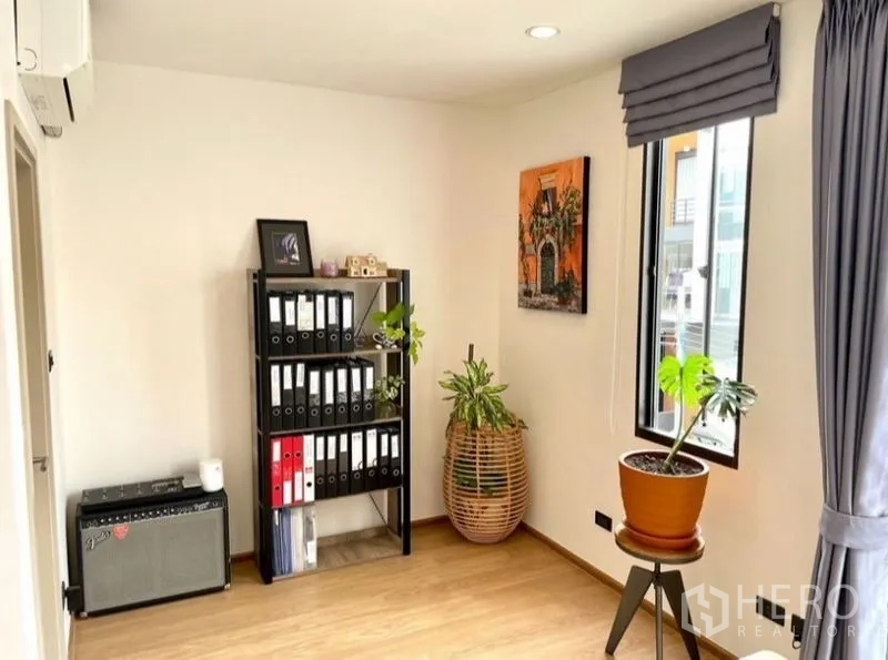 Townhouse for rent in Suan Luang, Bangkok - Office corner with shelving unit, window, and indoor plants.