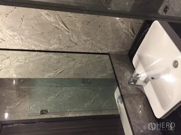 Condominium for sale in Watthana, Bangkok - Marble-tiled bathroom with glass shower enclosure and modern basin.