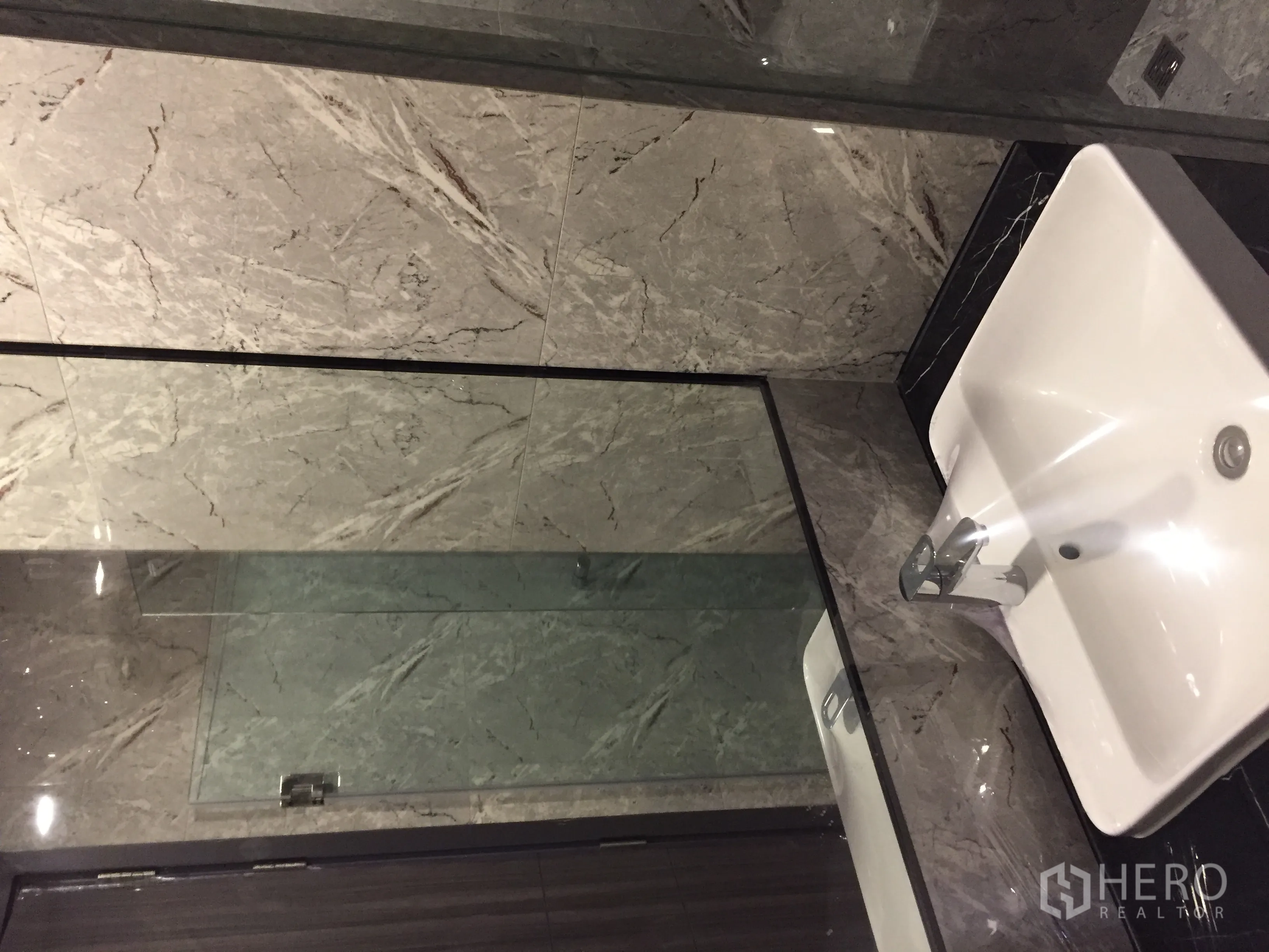 Condominium for sale in Watthana, Bangkok - Marble-tiled bathroom with glass shower enclosure and modern basin.