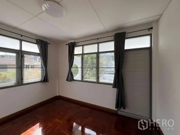 Detached House for rent in Bang Na, Bangkok - Corner bedroom with large windows, dark curtains and glossy parquet flooring.