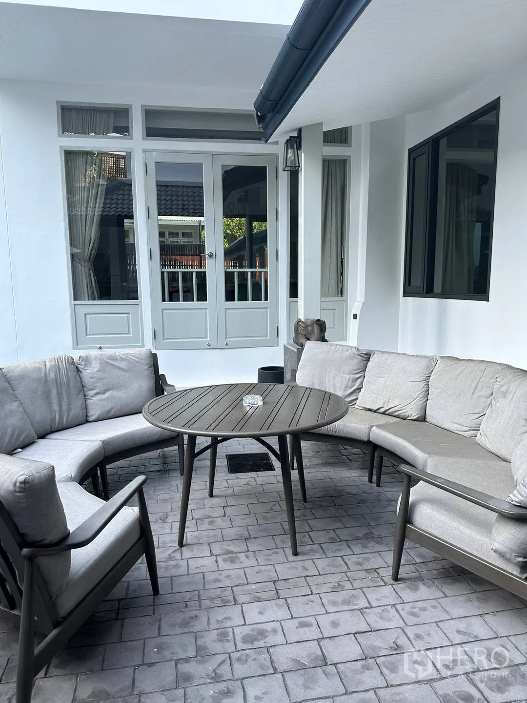 Detached House for rent in Watthana, Bangkok - Outdoor patio with curved sectional sofas and a round table by glass doors.