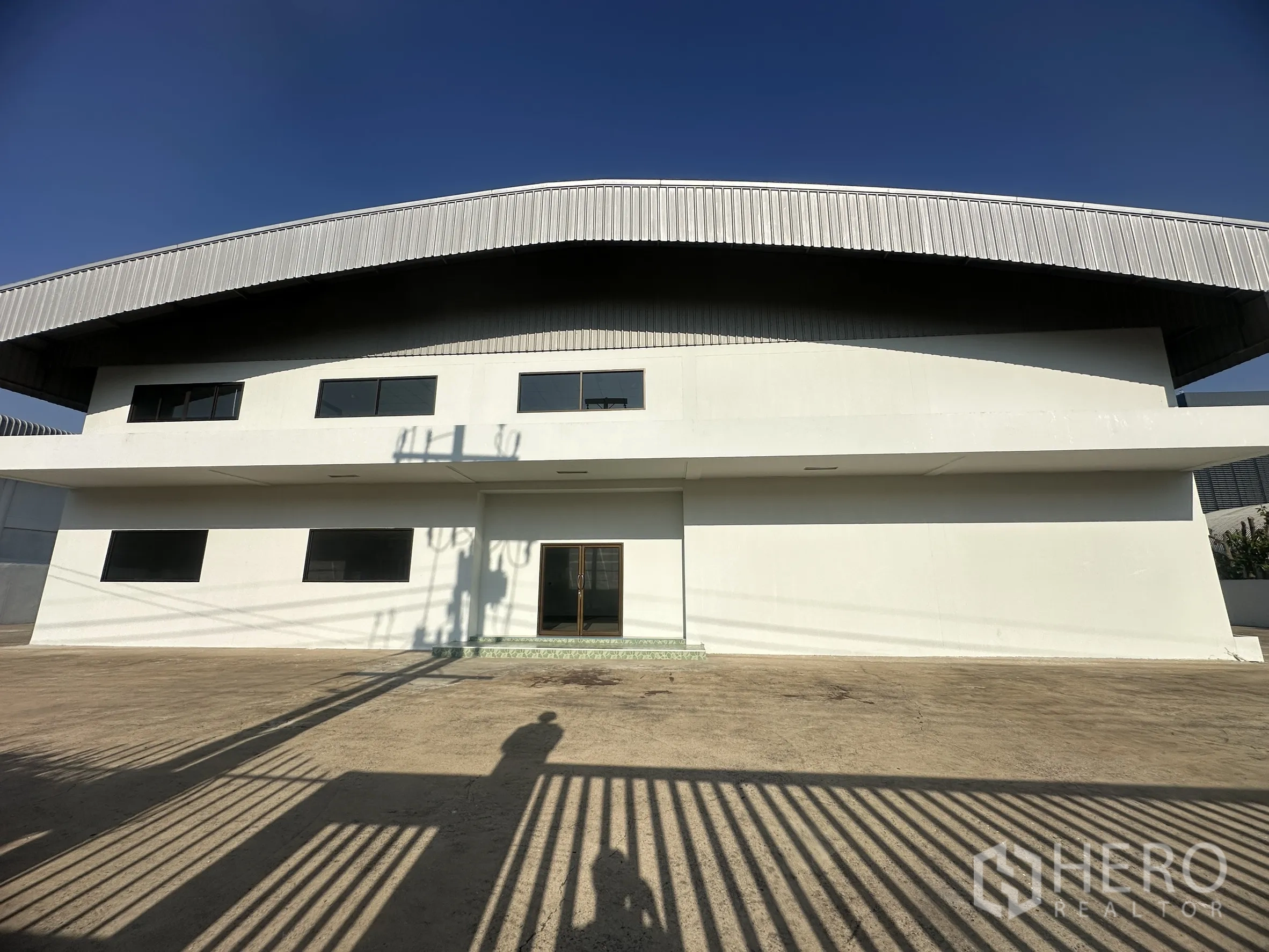 工厂 for sale in Khlong Luang, Pathum Thani - 厂房立面前的混凝土空地，配深色窗框。
