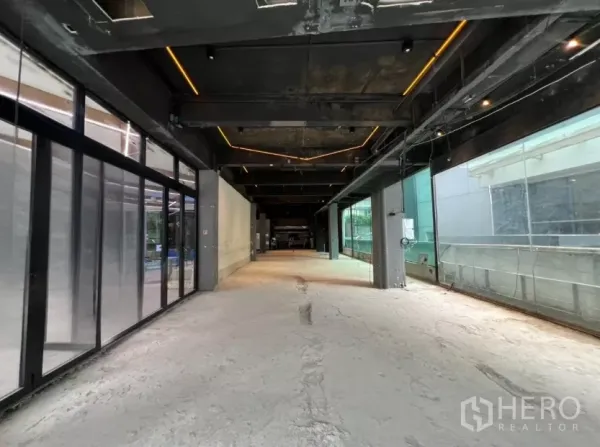 Retail Space for rent - Long open-plan retail interior with exposed black ceiling, LED strip lighting, concrete subfloor and large side windows.