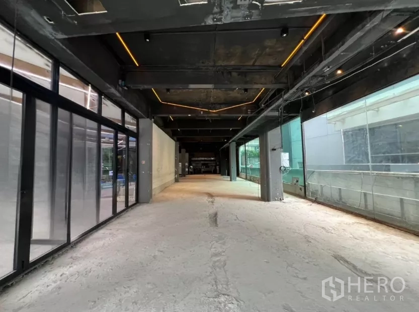 Retail Space for rent - Long open-plan retail interior with exposed black ceiling, LED strip lighting, concrete subfloor and large side windows.