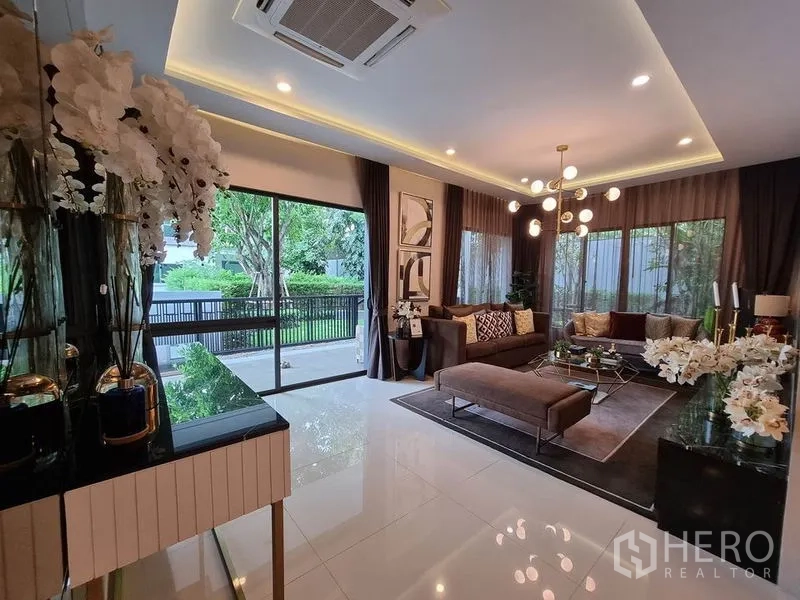 Detached House for rent in Prawet, Bangkok - Bright living room with sliding glass doors, statement chandelier and garden view.