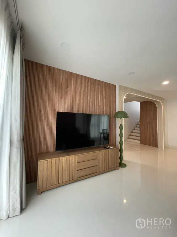 Detached House for rent in Bang Phli, Samut Prakan - Living room with wood-slat TV wall, low console, arched doorway and stairs in a Centro Bangna detached house.