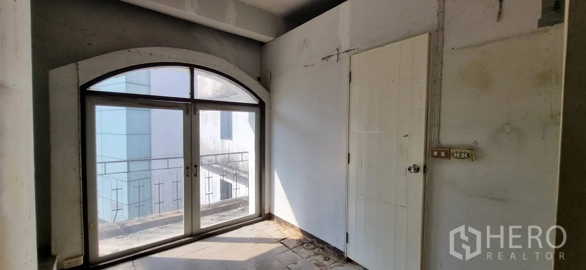 Shophouse for rent or sale in Bangkok - Small room with an arched sliding door to a balcony and weathered white walls.