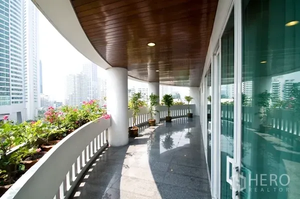 Apartment for rent in Khlong Toei, Bangkok - Curved balcony with planters, glass doors and skyline views of central Bangkok.