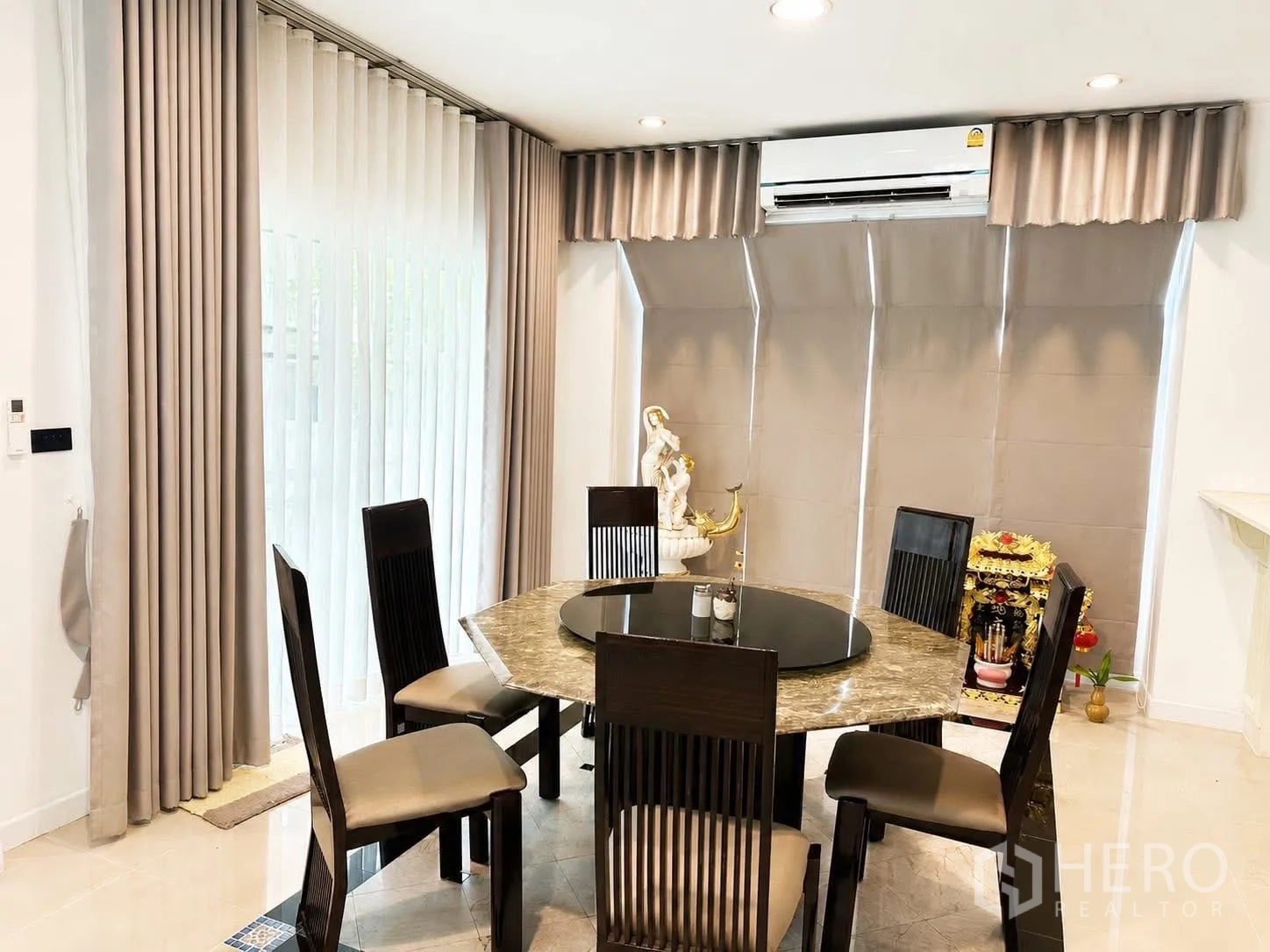 Detached House for rent in Prawet, Bangkok - Dining area with round marble table, six chairs, floor‑to‑ceiling windows, and air conditioner.