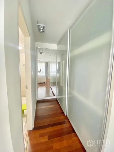 Condominium for rent in Watthana, Bangkok - Hallway with sliding frosted-glass wardrobe and wall mirror leading toward the bedroom.