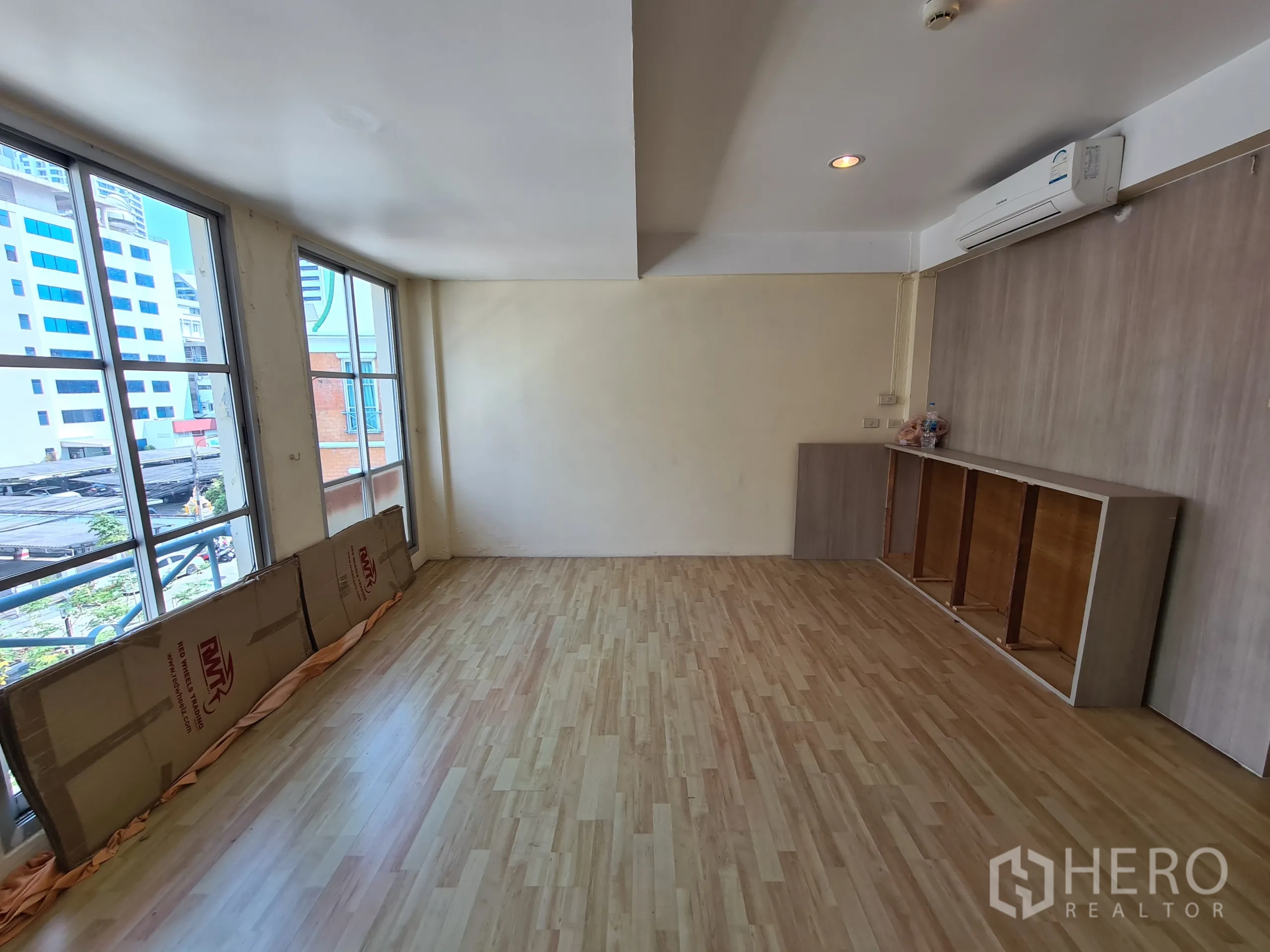 Shophouse for rent or sale in Sathon, Bangkok - Upper-floor room with wide windows and light wood laminate flooring overlooking nearby buildings.