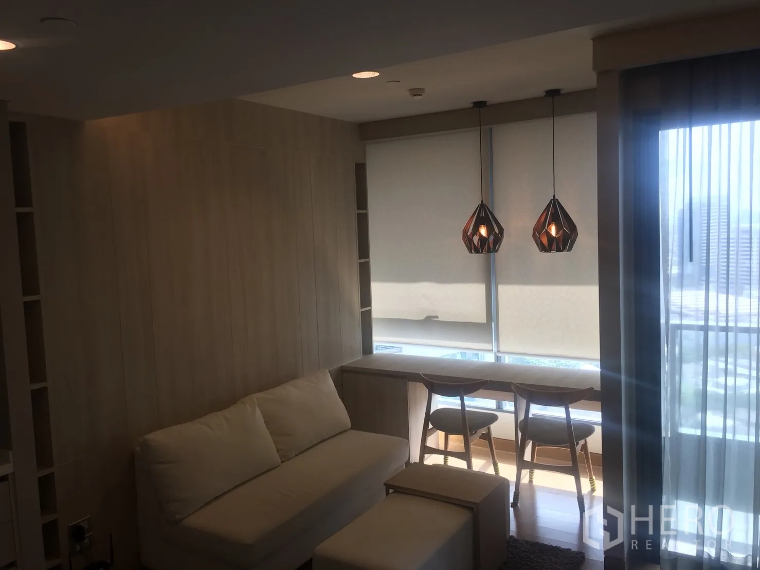 Condominium for rent in Khlong Toei, Bangkok - Bright living area with sofa, pendant lights, and window bar seating opening to a balcony with city views.