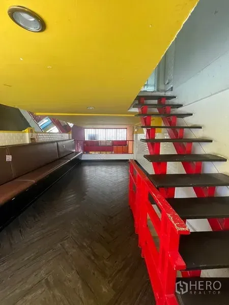 Shophouse for rent in Khlong Toei, Bangkok - Mezzanine level with red stairs and railing, built‑in bench seating and a yellow ceiling.