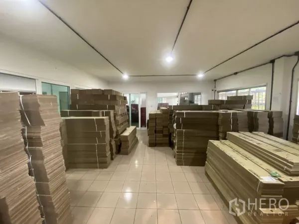 Factory for rent in Mueang Nakhon Pathom, Nakhon Pathom - Bright storage room with stacks of flat cardboard on a tiled floor and windows.
