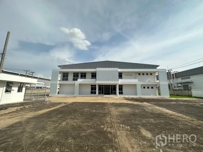 Factory for rent in Phra Nakhon Si Ayutthaya - Front facade of factory with secure gate and expansive concrete apron for truck maneuvering.