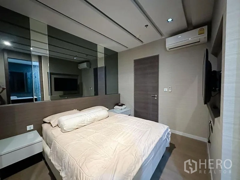 Condominium for rent or sale in Khlong Toei, Bangkok - Cozy bedroom with bed, mirrored wall, air conditioner and wall-mounted TV.